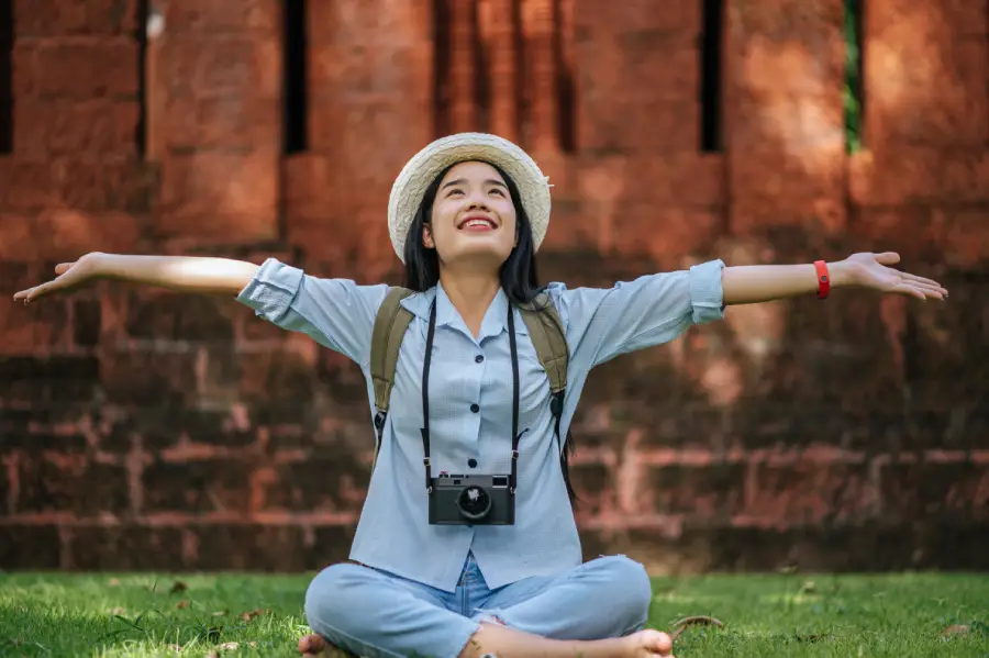 young-asian-backpacker-female-wearing-hat-smiling-while-has-trip-historic-site-she-sitting-grass-relaxing-use-camera-take-photo-with-happy